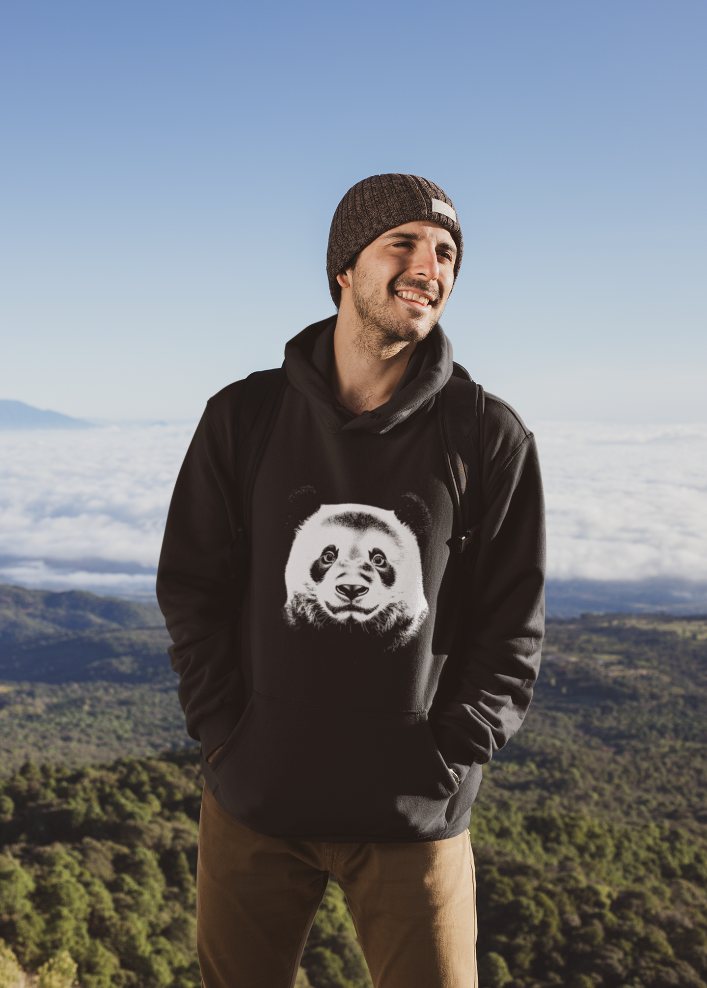 Man wearing a black hoodie with a panda design, standing in a scenic outdoor setting.